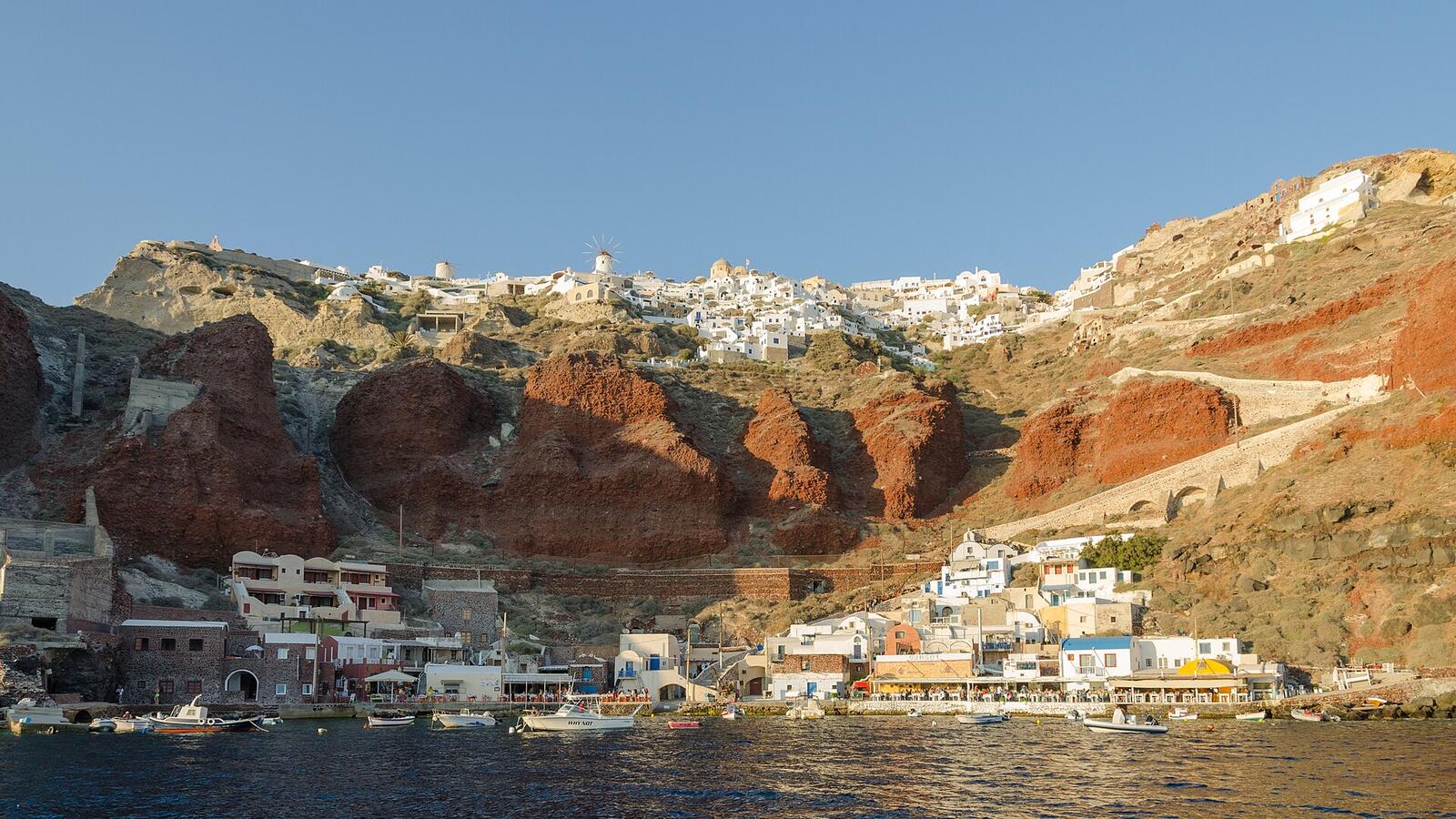 Oia vanaf een boot in de caldera met witte huizen op de rode rotsen
