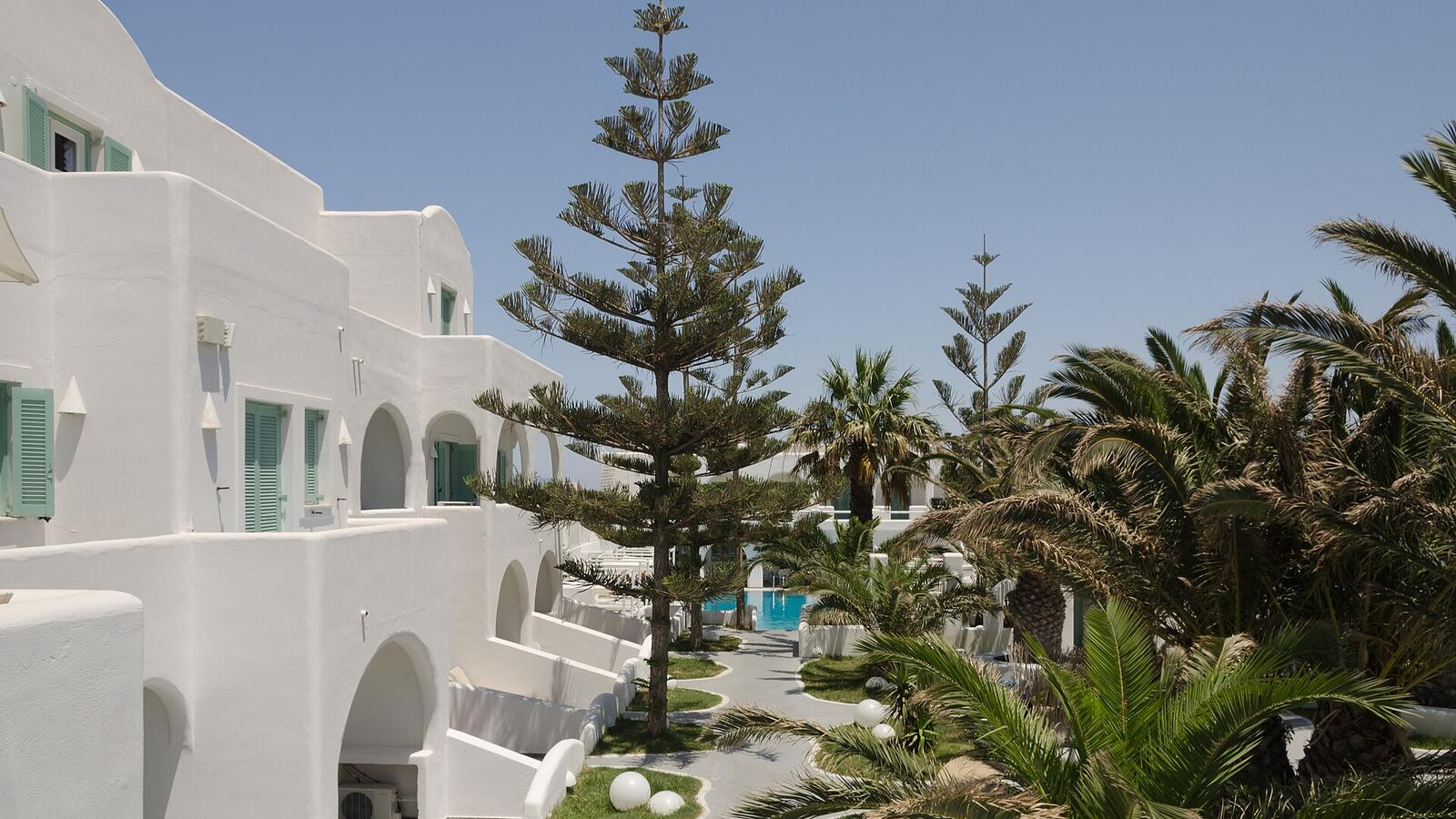 Hotel met witte gebouwen, palmbomen en een zwembad in Fira